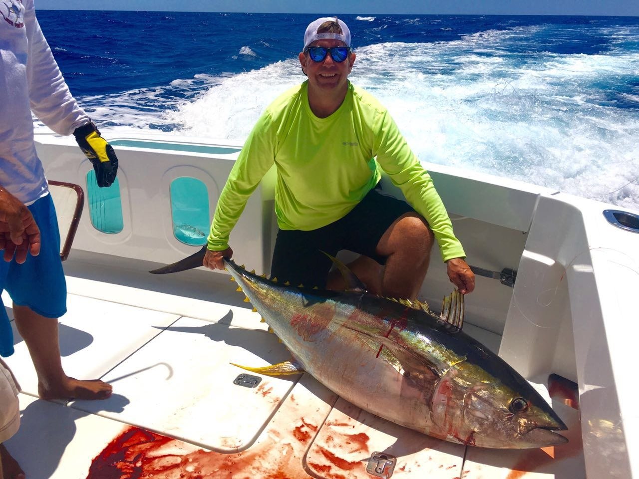 Jay Christopher Humphreys kneeling on a fishing boat holding a large tuna, open ocean wake behind him.