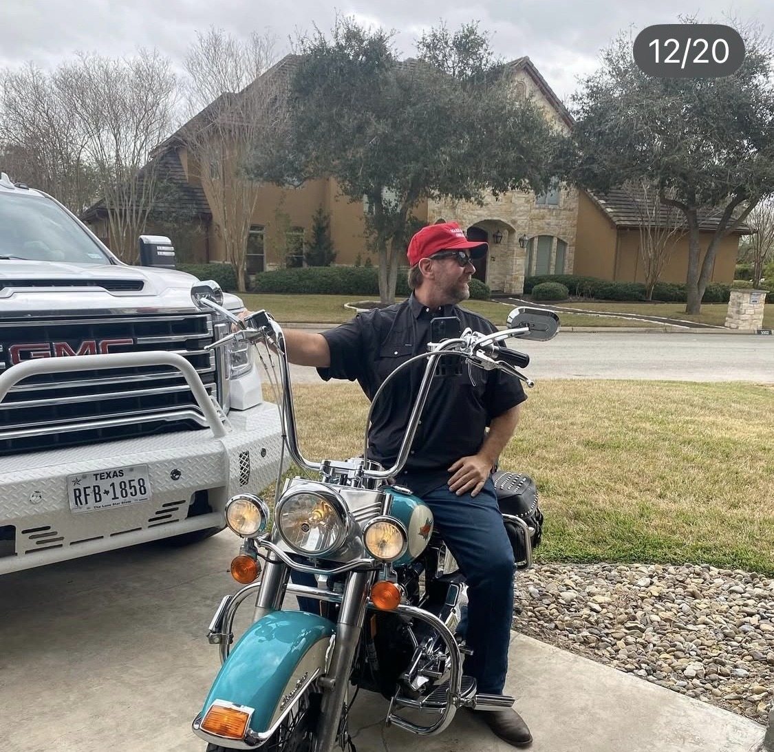 Jay Christopher Humphreys wearing a red cap, seated on a teal motorcycle in a residential driveway beside a white truck.