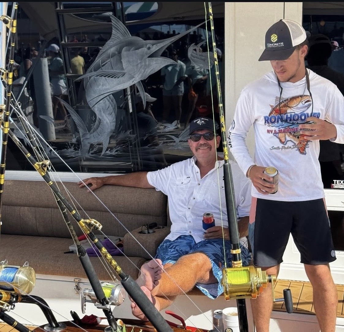 Jay Christopher Humphreys seated on a sport-fishing boat at South Padre Island, Texas, with fishing rods and a companion standing nearby.
